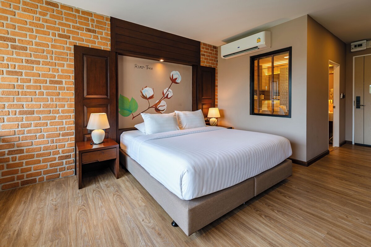 A hotel room with a brick wall, a bed with white linens, two bedside tables with lamps, and an air conditioning unit.