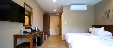 A hotel room with a bed, a desk with a chair, a flat-screen TV mounted on the wall, and an air conditioning unit.