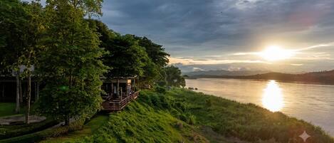 A riverside view with a wooden structure overlooking the water, surrounded by lush greenery.