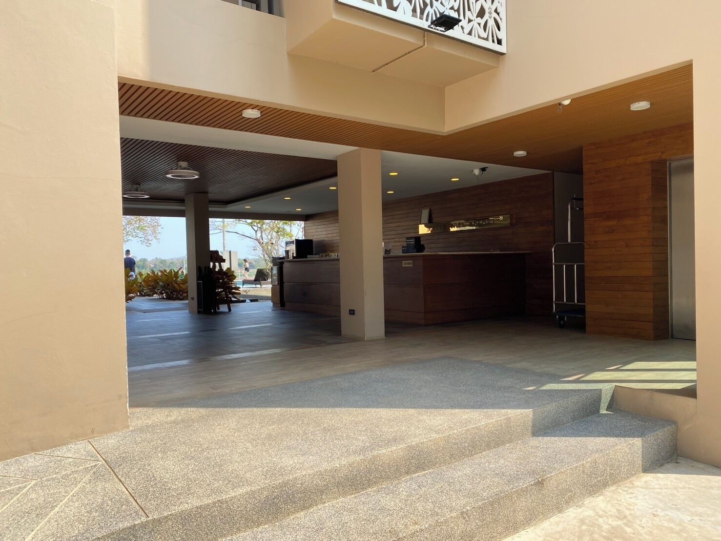 Eine moderne Hotelhalle mit Empfangstresen, einer Treppe und Blick ins Freie.