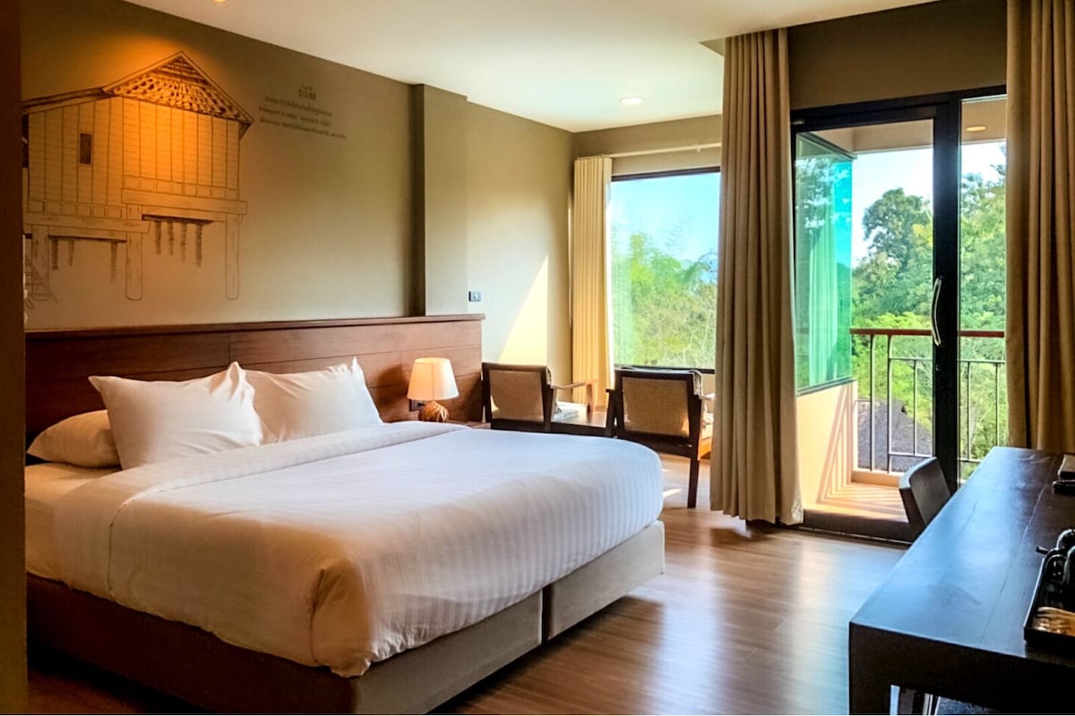 A hotel room with a large bed, a desk, and a balcony with a view of the outdoors.