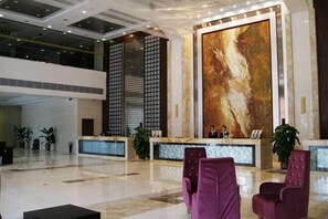 Een ruime lobby met een receptiebalie, een zithoek en een groot abstract schilderij aan de muur.