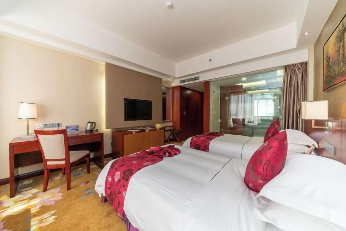 A hotel room with two beds, a desk, a chair, a television, and a large mirror.
