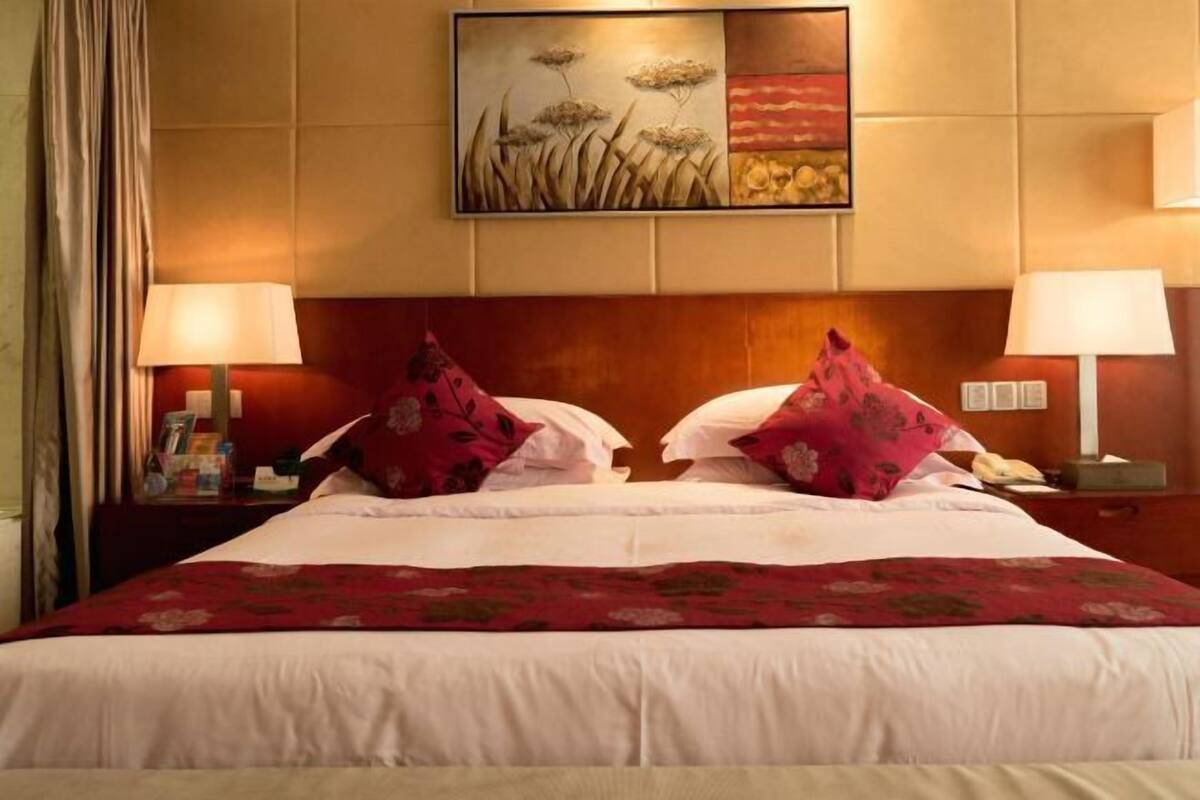 Une chambre d’hôtel avec un grand lit, deux lampes de chevet, une table de chevet avec un téléphone et un tableau au mur.