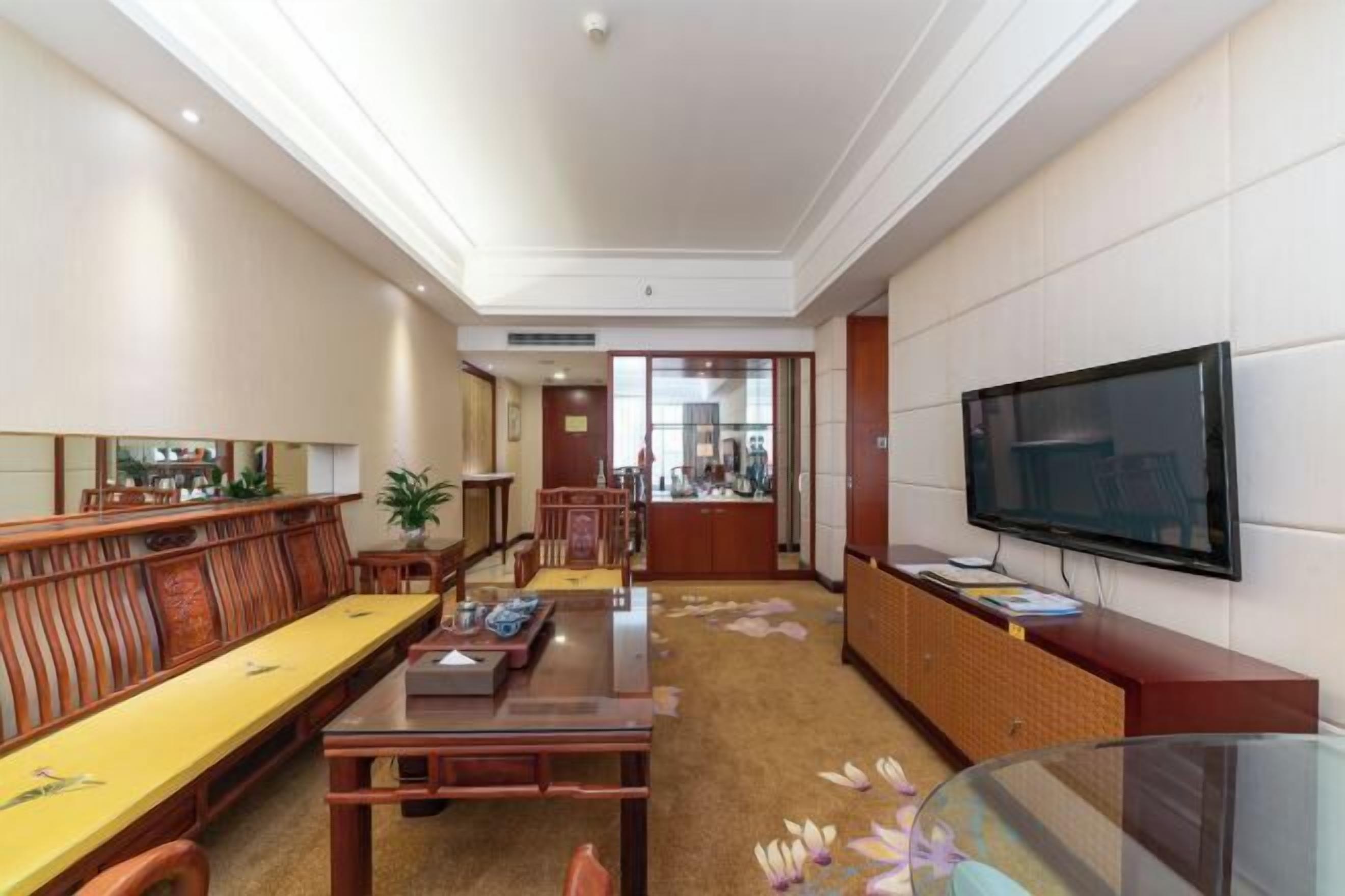 A hotel room with a wooden dining table, a sofa, a TV, and a cabinet.