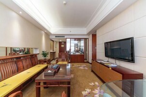 A hotel room with a wooden dining table, a sofa, a TV, and a cabinet.