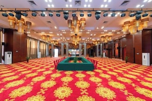 Un amplio salón con alfombra estampada, una mesa verde en el centro y una fila de puertas en un lateral.