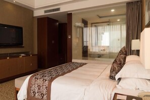 A hotel room with a large bed, a television on the wall, a wardrobe, and a glass door leading to a bathroom. - Xiangcheng International Hotel (Pingxiang)