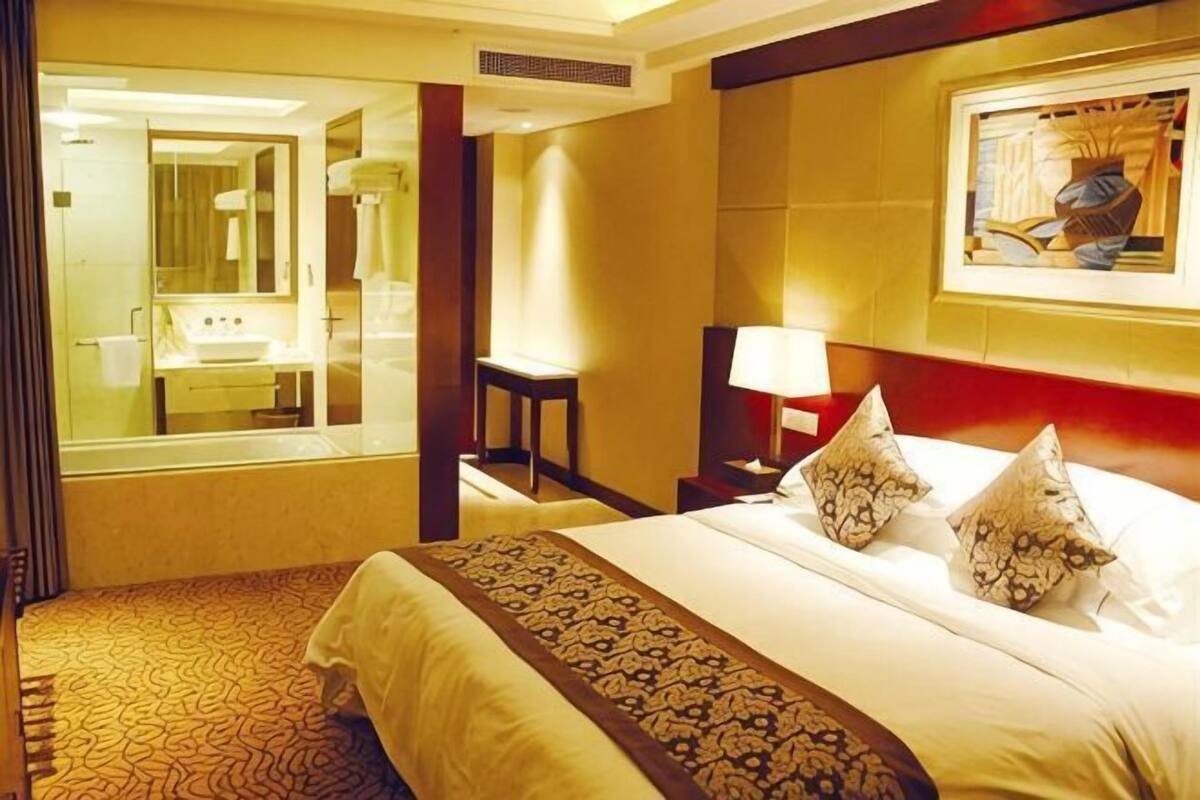 Une chambre d’hôtel avec un grand lit, un miroir dans la salle de bain, une table de chevet et un tableau au mur.