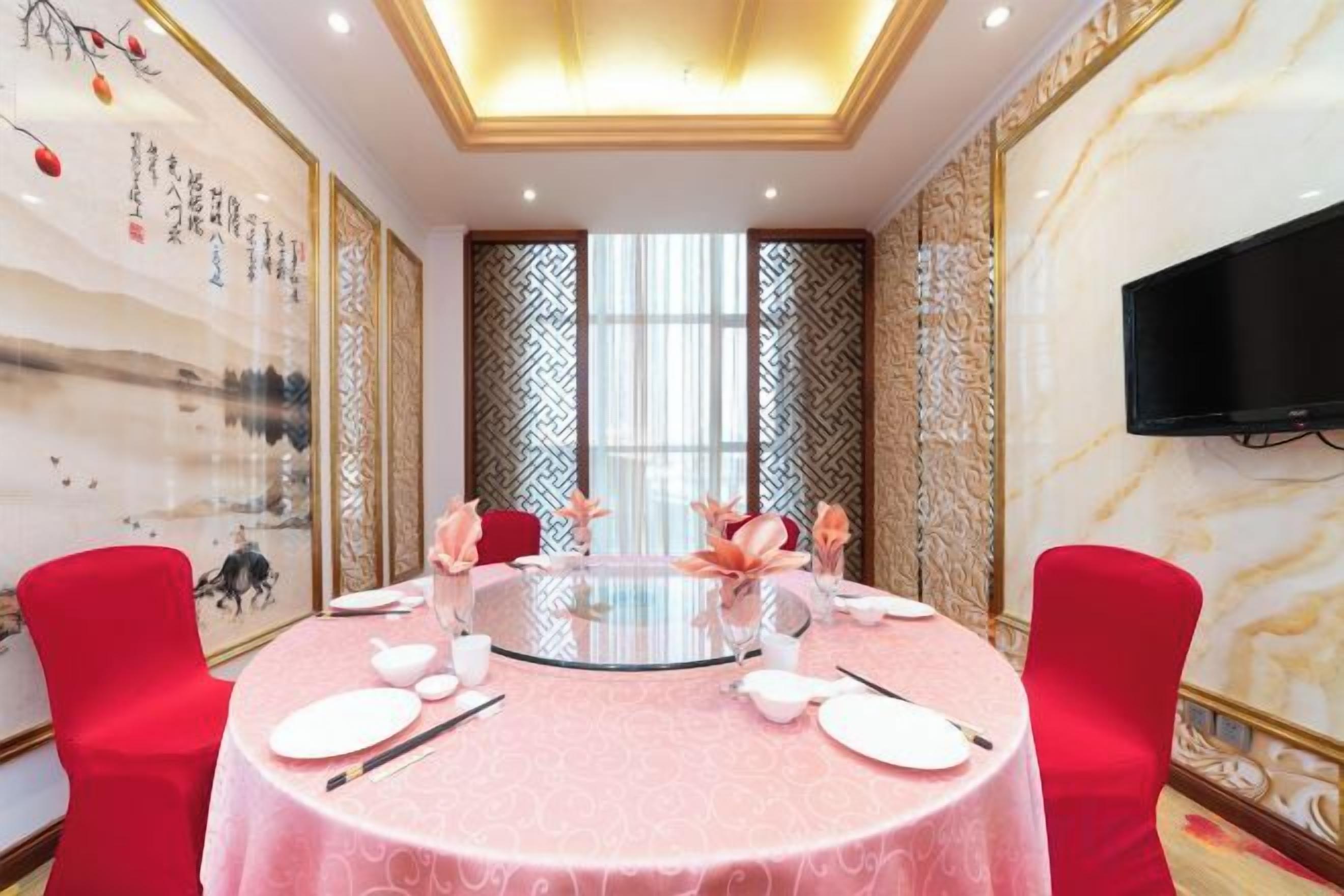 A round table with a pink tablecloth, red chairs, and a glass centerpiece.