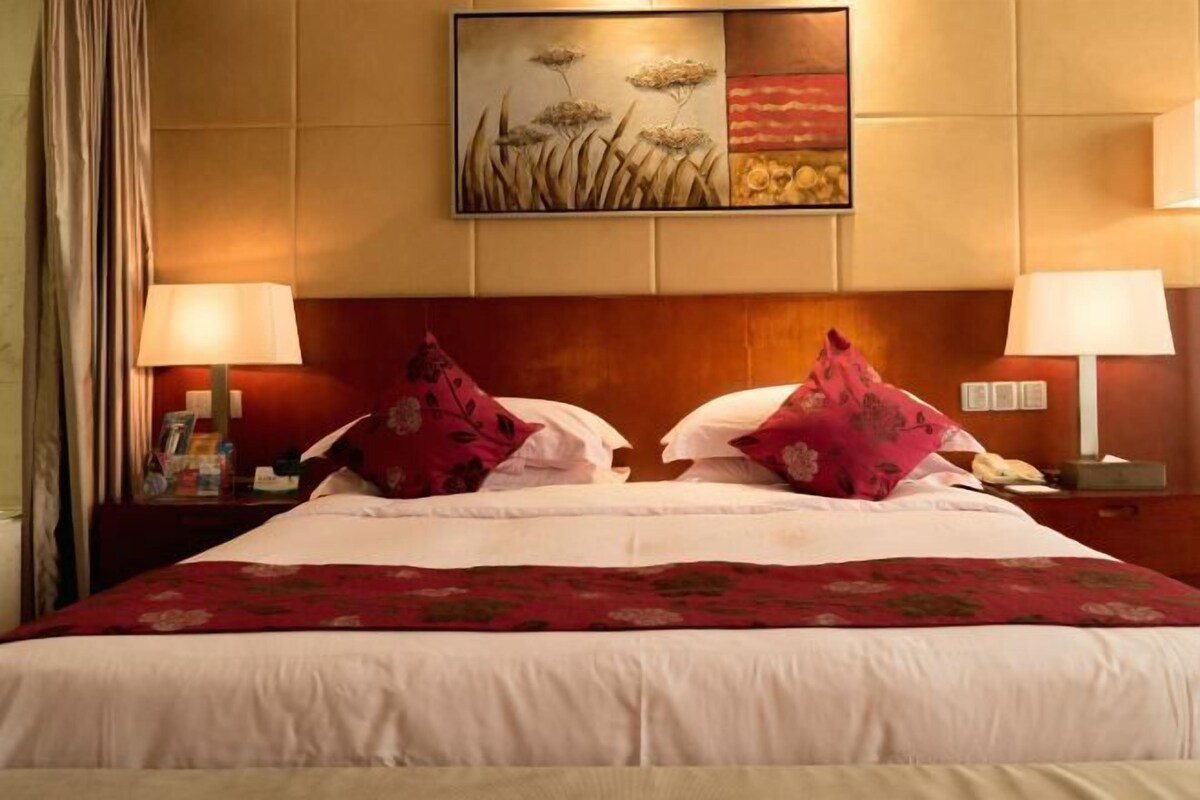A hotel room with a large bed, two bedside lamps, a nightstand with a telephone, and a painting on the wall.