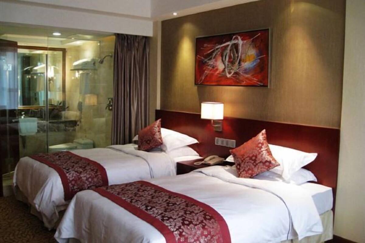 Une chambre d’hôtel avec deux lits, une douche en verre, un tableau au mur et une lampe de chevet.