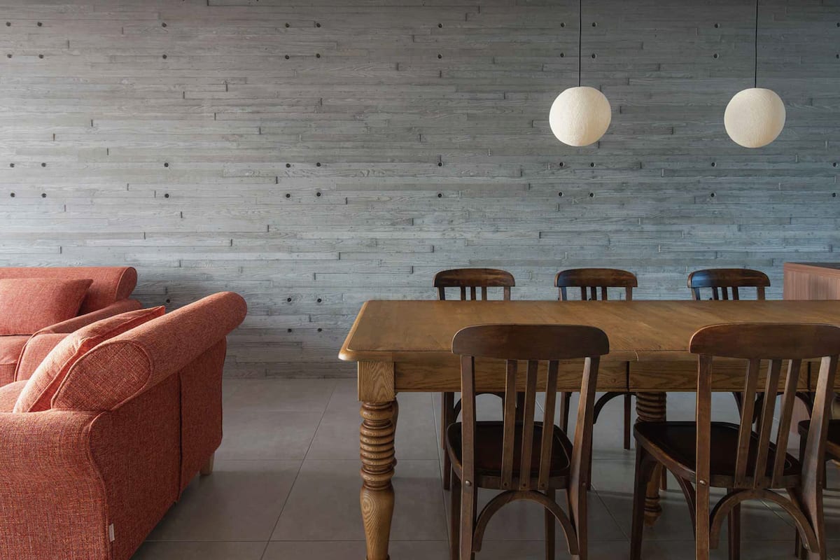 A dining area with a wooden table and chairs, a red sofa, and a grey textured wall.
