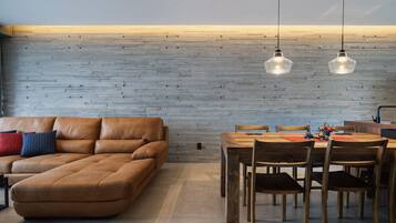 A modern living room with a brown leather sofa, wooden dining table, and chairs.