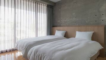 Una habitación de hotel moderna con dos camas, una pared de acento de concreto y ventanas amplias con cortinas traslúcidas.