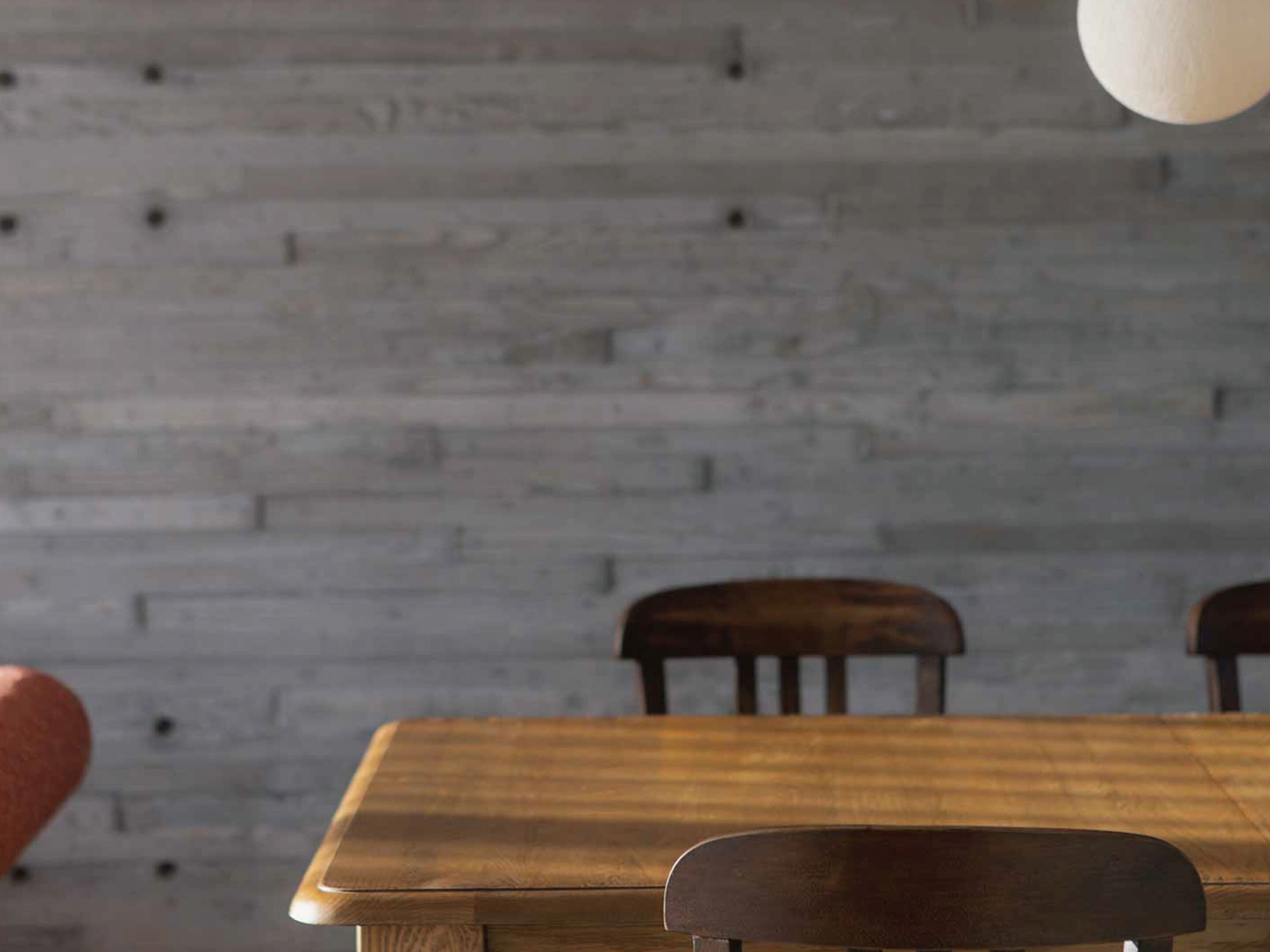 A wooden dining table with chairs in a room with a grey brick wall.