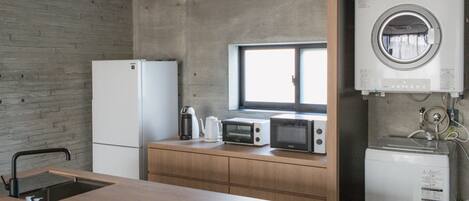 A compact kitchen with a refrigerator, microwave, kettle, and a built-in oven.