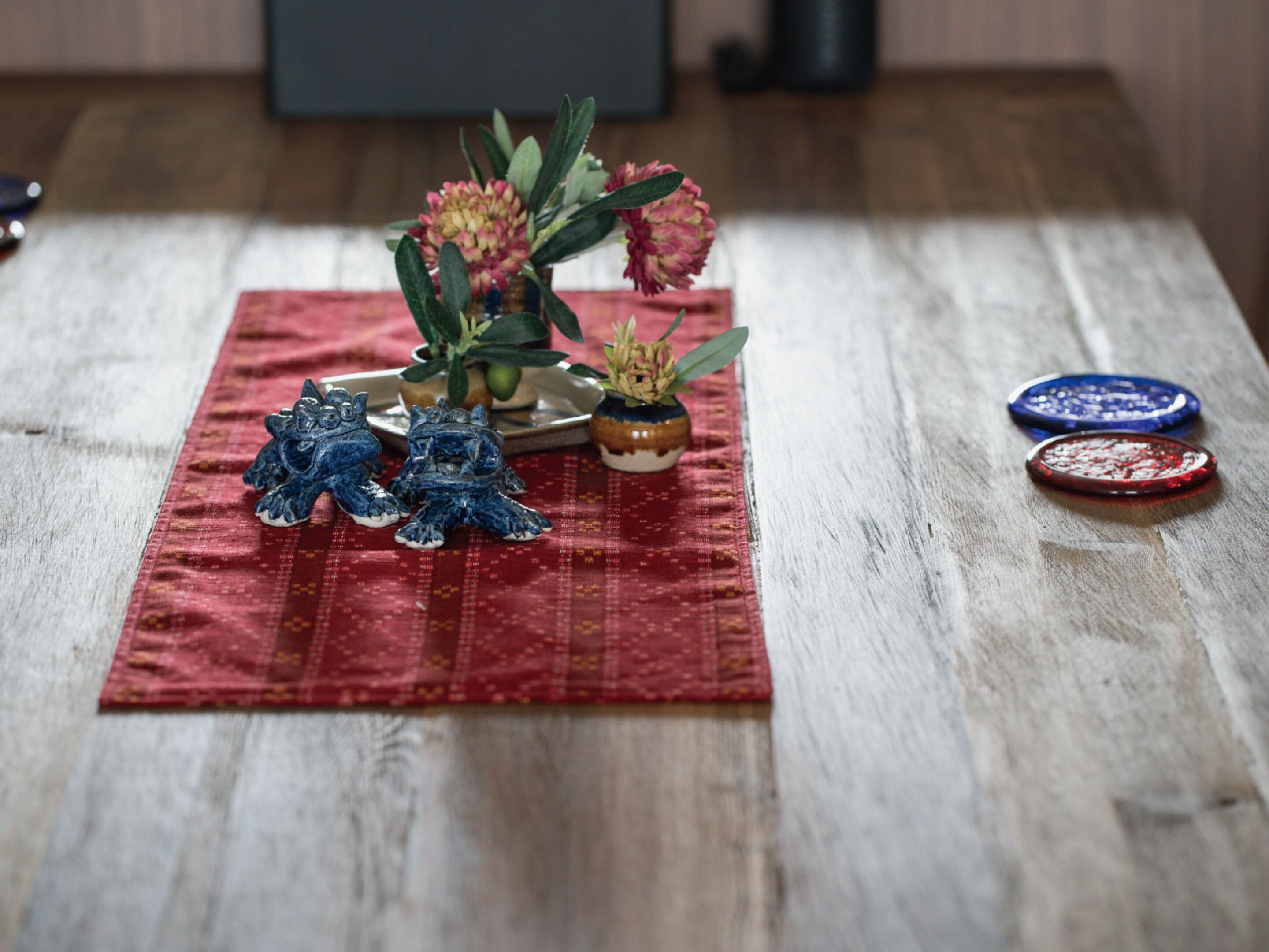 A wooden table with a red cloth, two blue and one red decorative plate, and three small ceramic frog figurines.