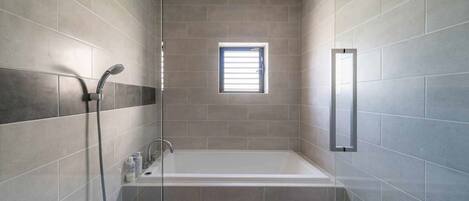 A modern bathroom with a bathtub, shower, and a window.
