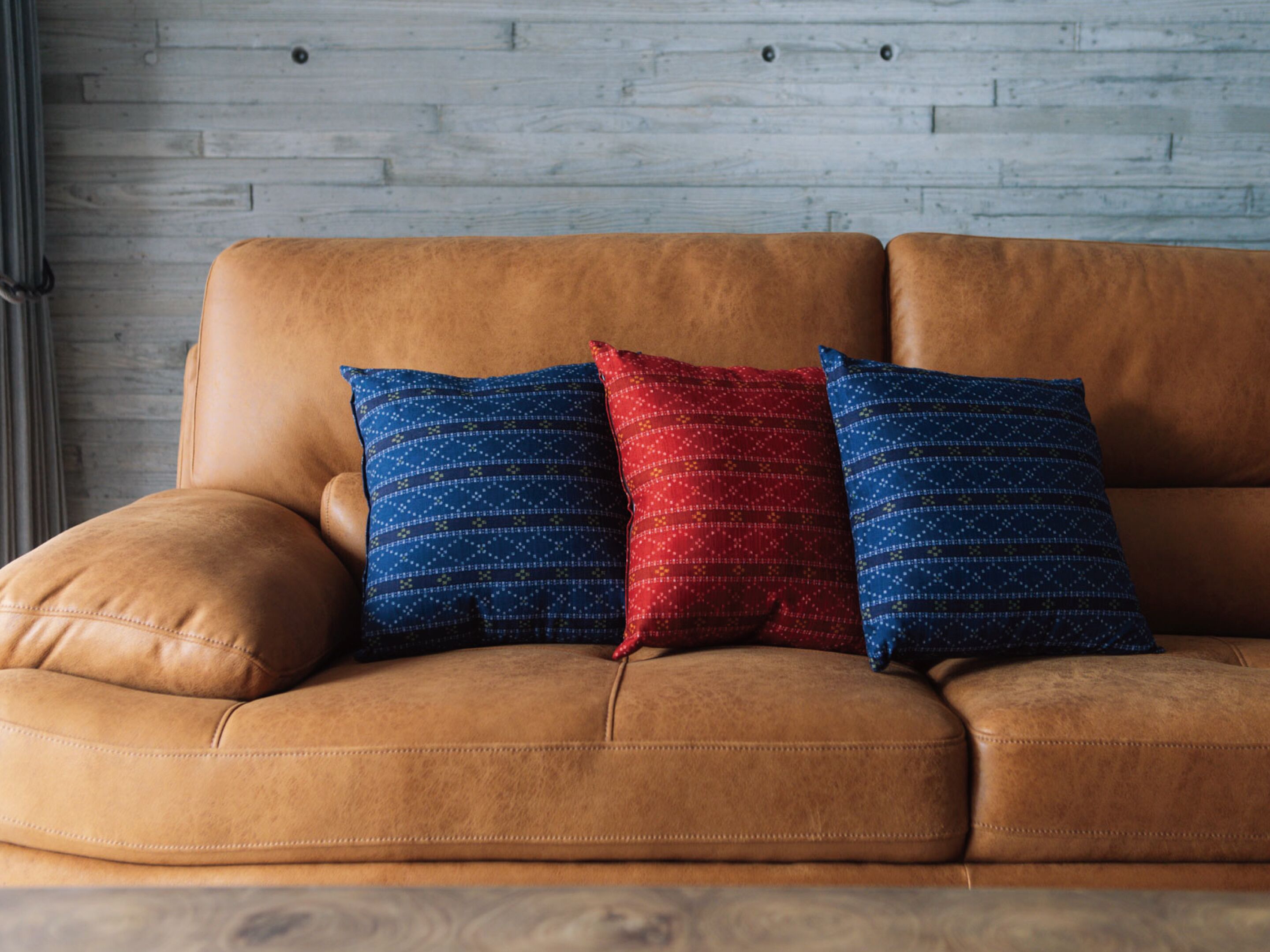 Ein braunes Ledersofa mit drei Kissen in Blau, Rot und Blau.