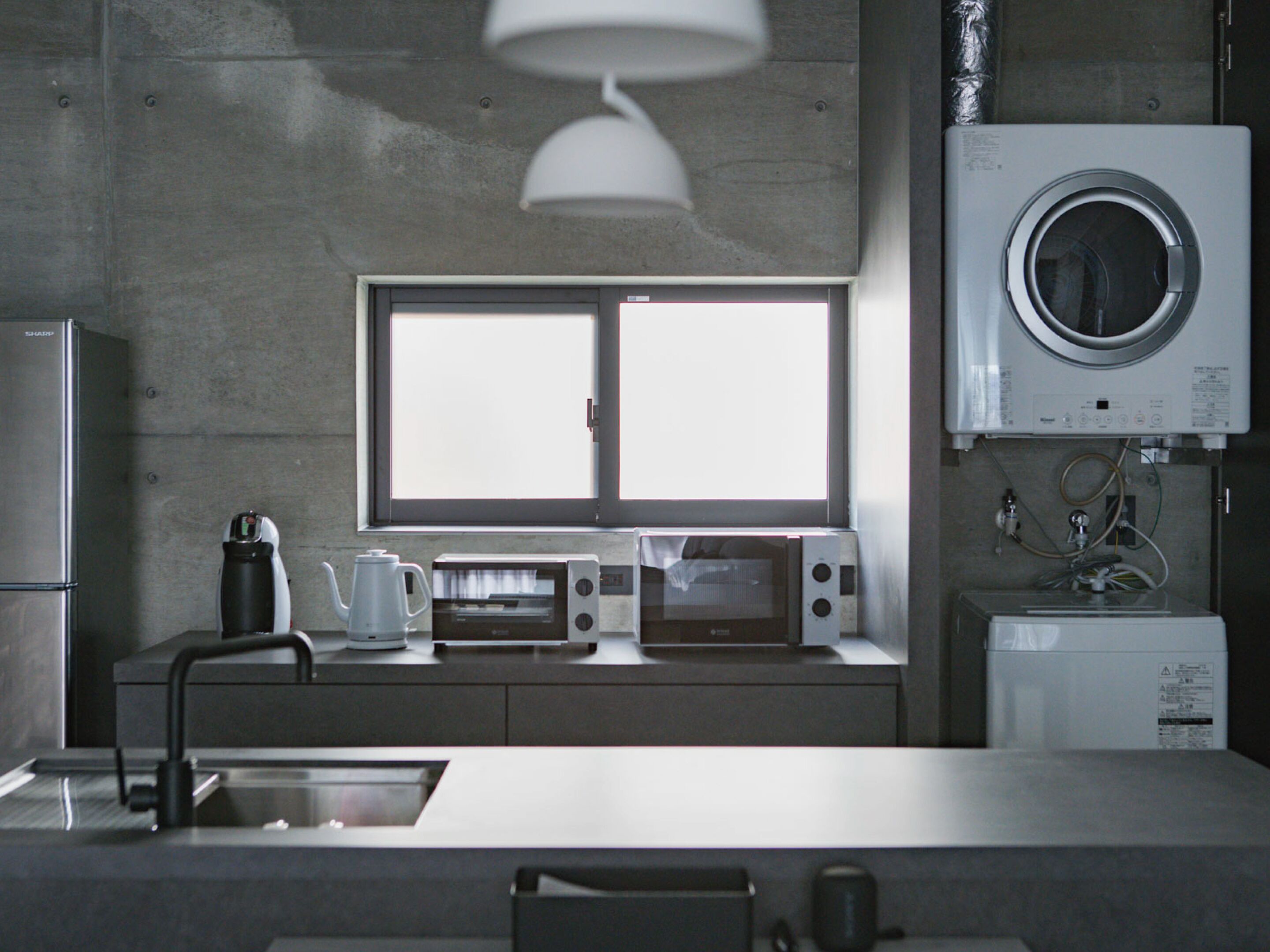 A modern kitchen with a built-in oven, a coffee maker, a microwave, and a window above the sink.