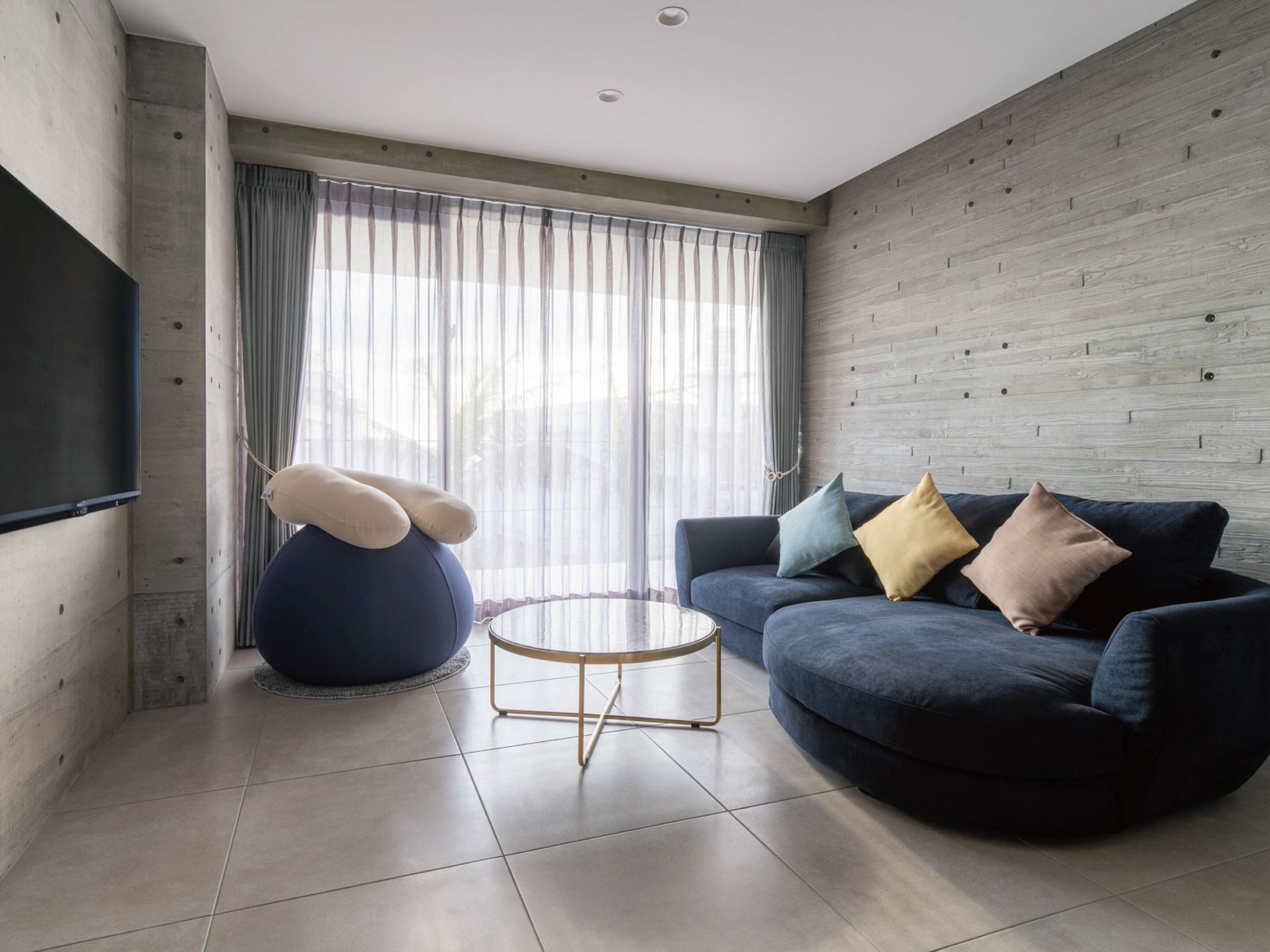 Uma sala de estar moderna com um sofá azul escuro, uma mesa de centro redonda e um grande puff.