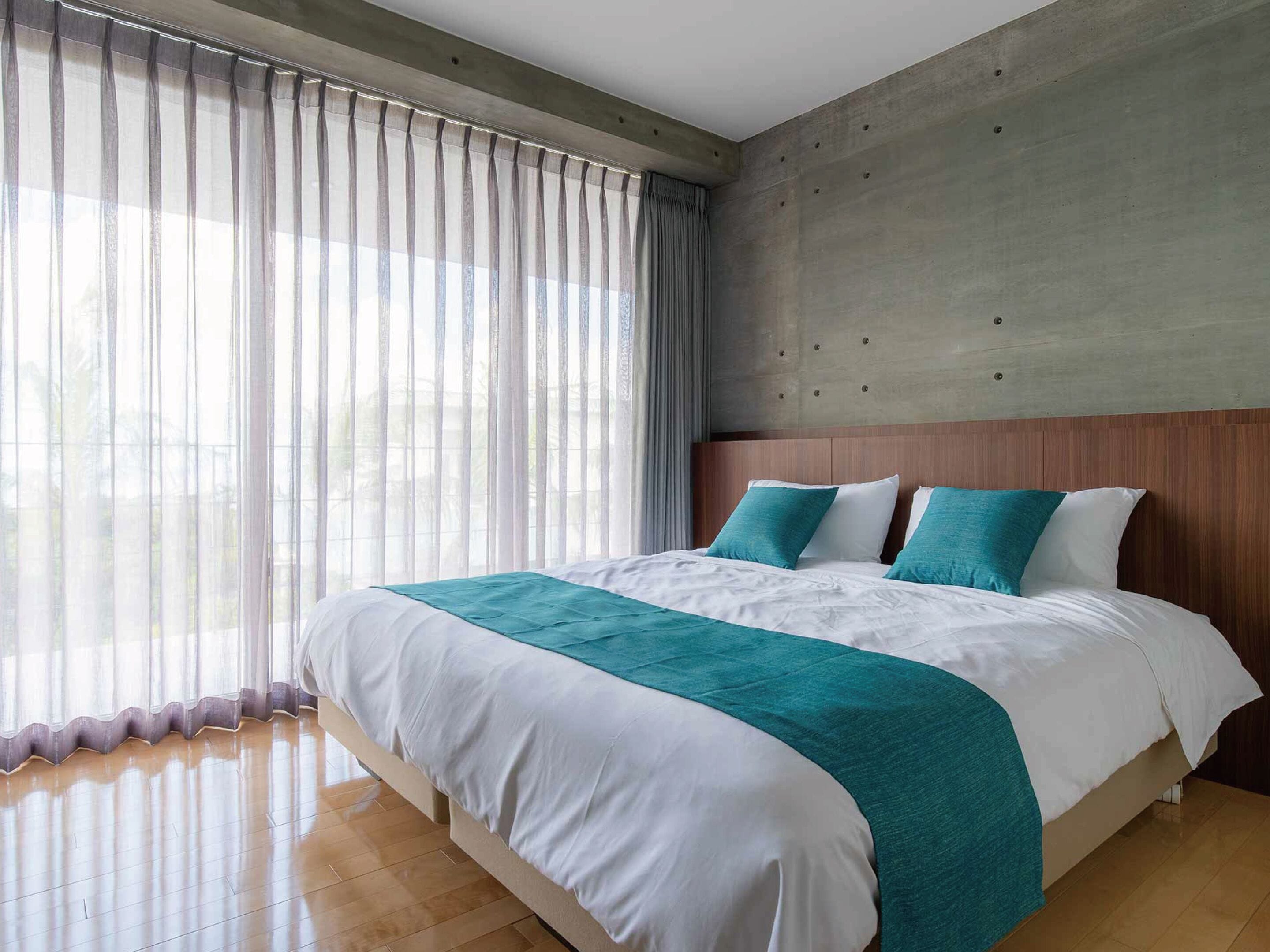 Camera d'albergo moderna con un letto grande, una parete d'accento in cemento e tende leggere.