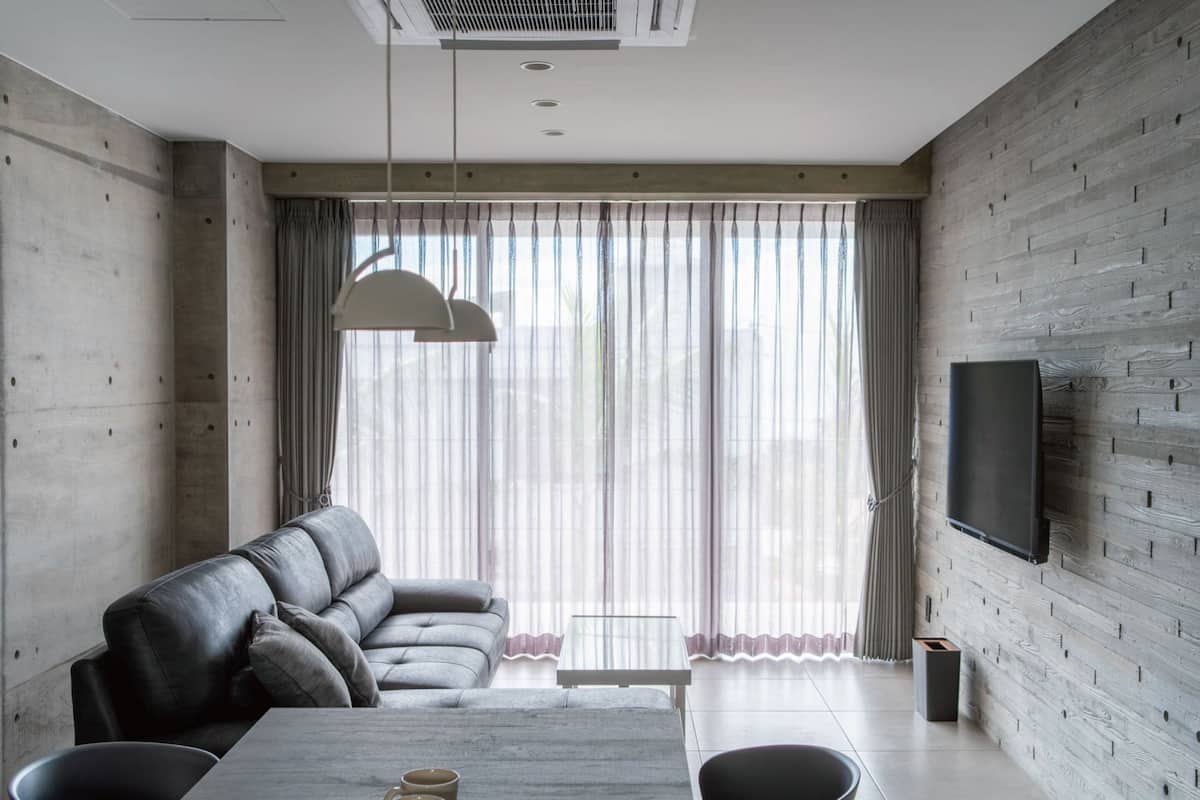 A modern living room with a sofa, dining table, chairs, and a TV mounted on a wooden wall.