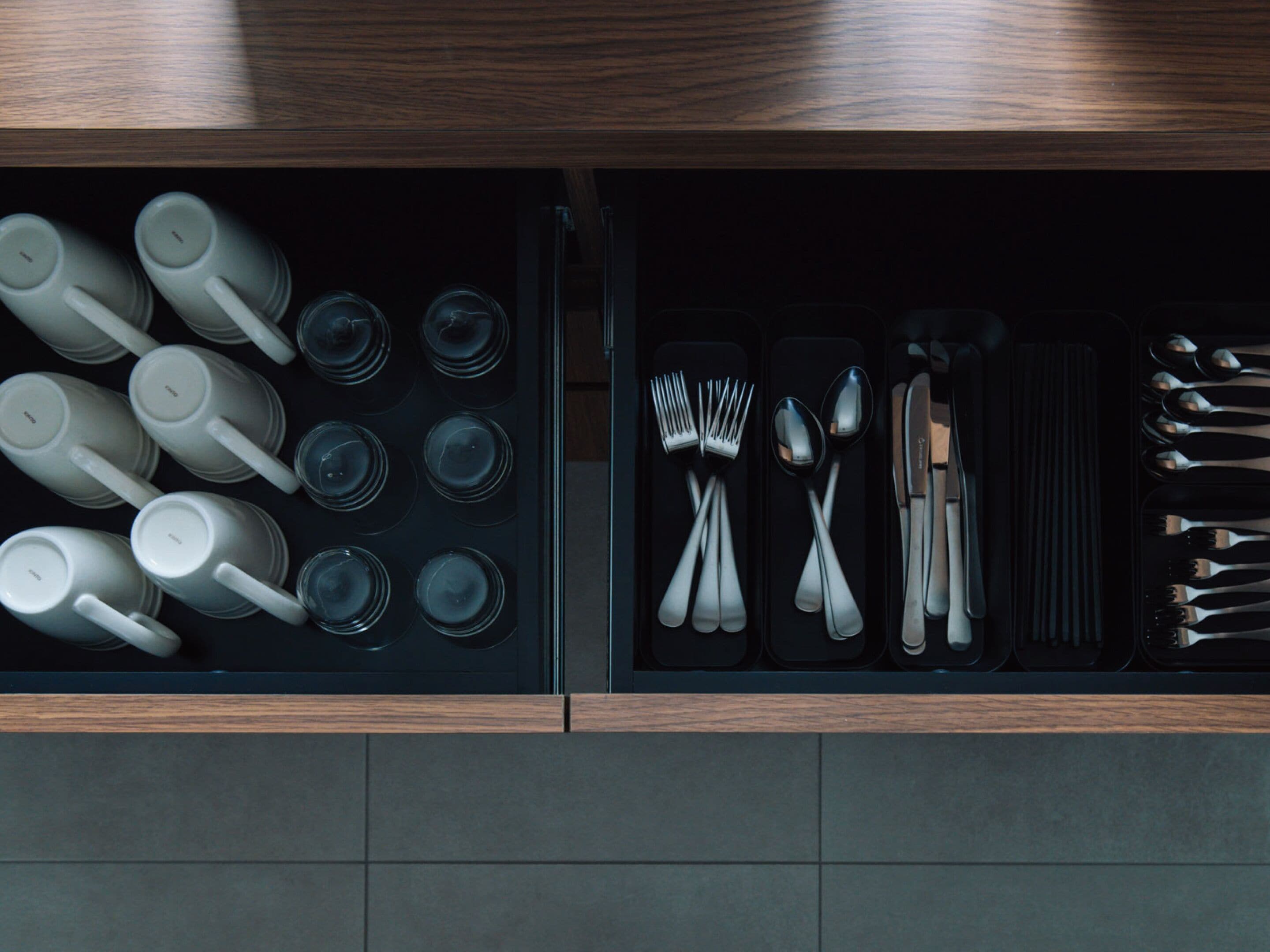 A kitchen drawer with neatly organized utensils and cookware, including mugs, spoons, forks, and knives.