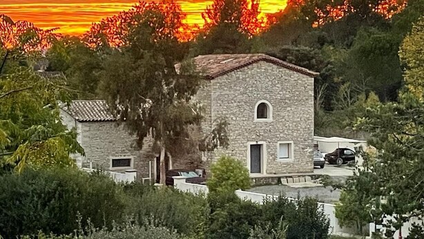 Un edificio de piedra con techo de tejas, rodeado de vegetación y árboles.
