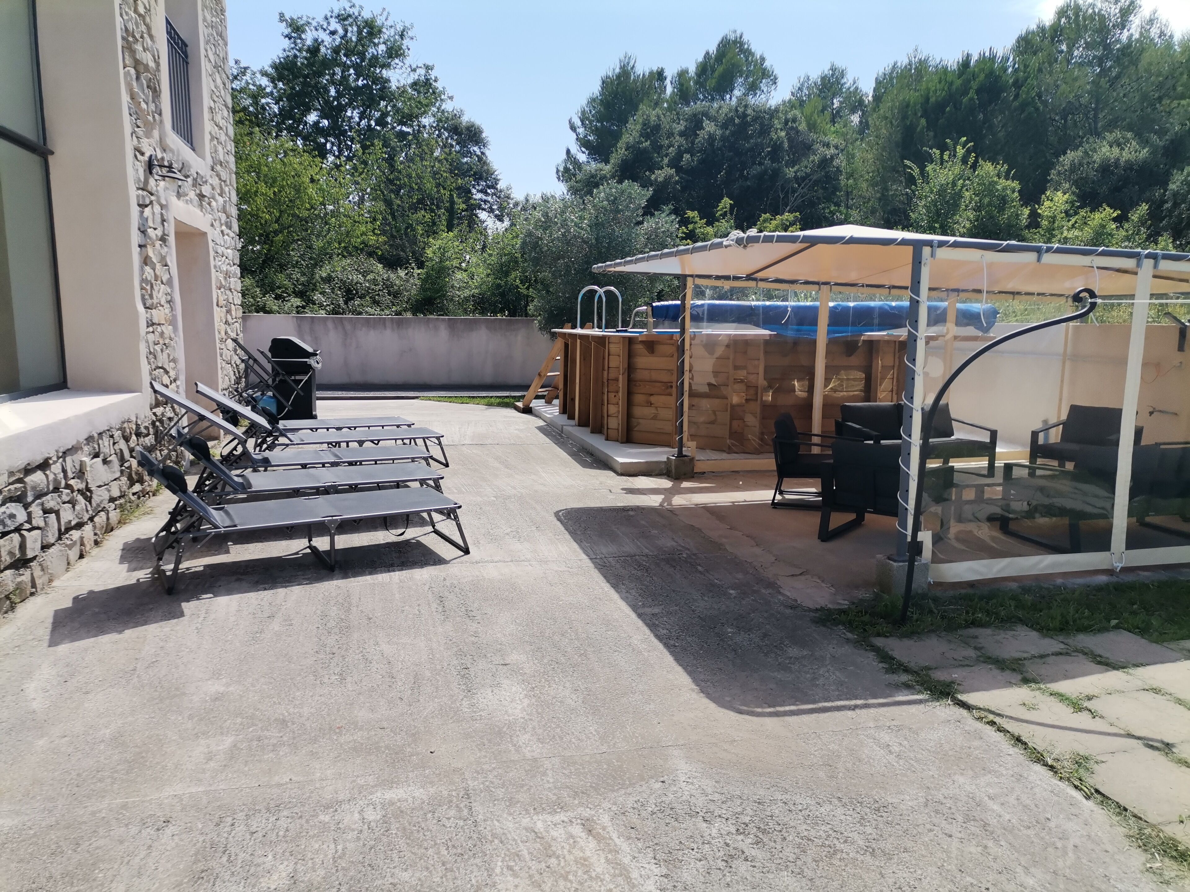 Eine Terrasse mit Sitzgelegenheiten im Freien, einer überdachten Grillstelle und einem Pool.