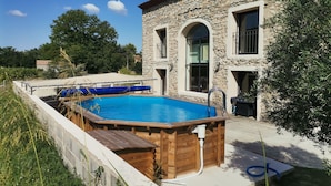 Un edificio de piedra con piscina, terraza de madera y una manguera conectada a la piscina.