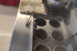 Un electrodoméstico de acero inoxidable con cuatro moldes redondos para cocinar, un colador metálico y una cesta tejida.