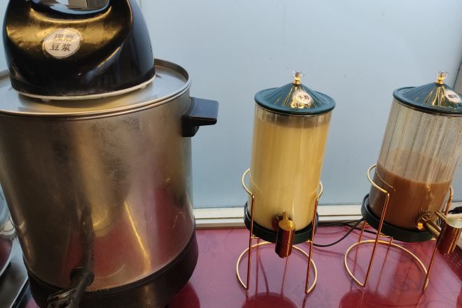 A coffee maker with a black top and a stainless steel body, a glass carafe with a gold-colored liquid, and a smaller glass container with a brown liquid.