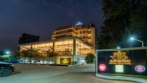 Un hôtel moderne doté d’une façade en verre, d’une enseigne lumineuse et d’une entrée agrémentée de jardins.