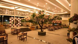 Un vaste espace intérieur aménagé avec de nombreux coins salon, un arbre décoratif central et un bar situé au fond de la pièce.
