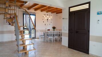 A spacious living area with a wooden staircase, a dining table with chairs, and a dark wooden door.