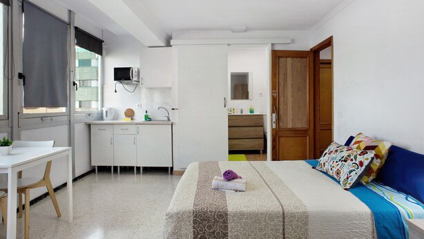Quarto com cama, mesa de cabeceira e vista para a cozinha.