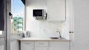 Uma cozinha moderna com armários brancos, micro-ondas embutido, chaleira e pia.