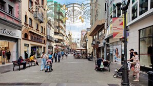 Rua de pedestres repleta de lojas e cafés, com bancos e pessoas caminhando.