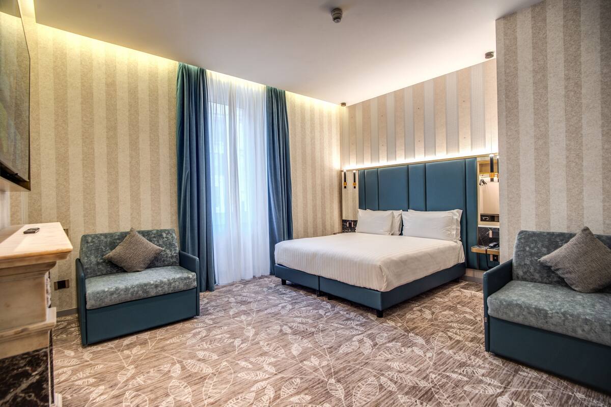 A hotel room with a large bed, two sofas, a desk, and a patterned carpet.