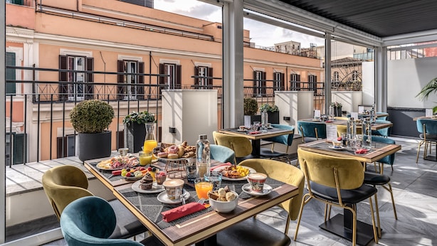 A rooftop dining area with tables set for breakfast, overlooking a cityscape. - CC Palace Hotel Roma (Rome)
