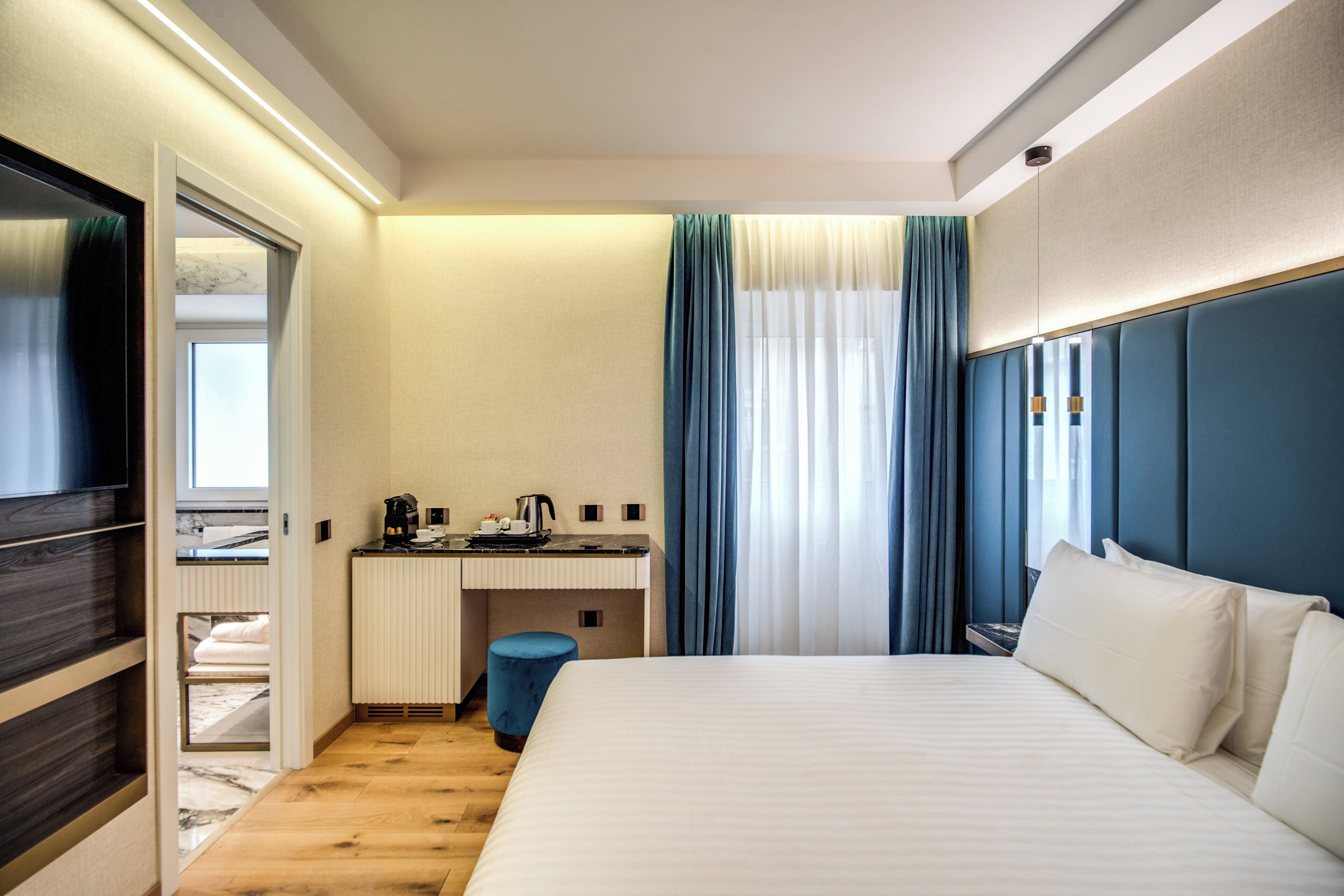 Une chambre d’hôtel équipée d’un lit, d’un bureau, d’une chaise, d’une petite poubelle et d’une fenêtre avec des rideaux.