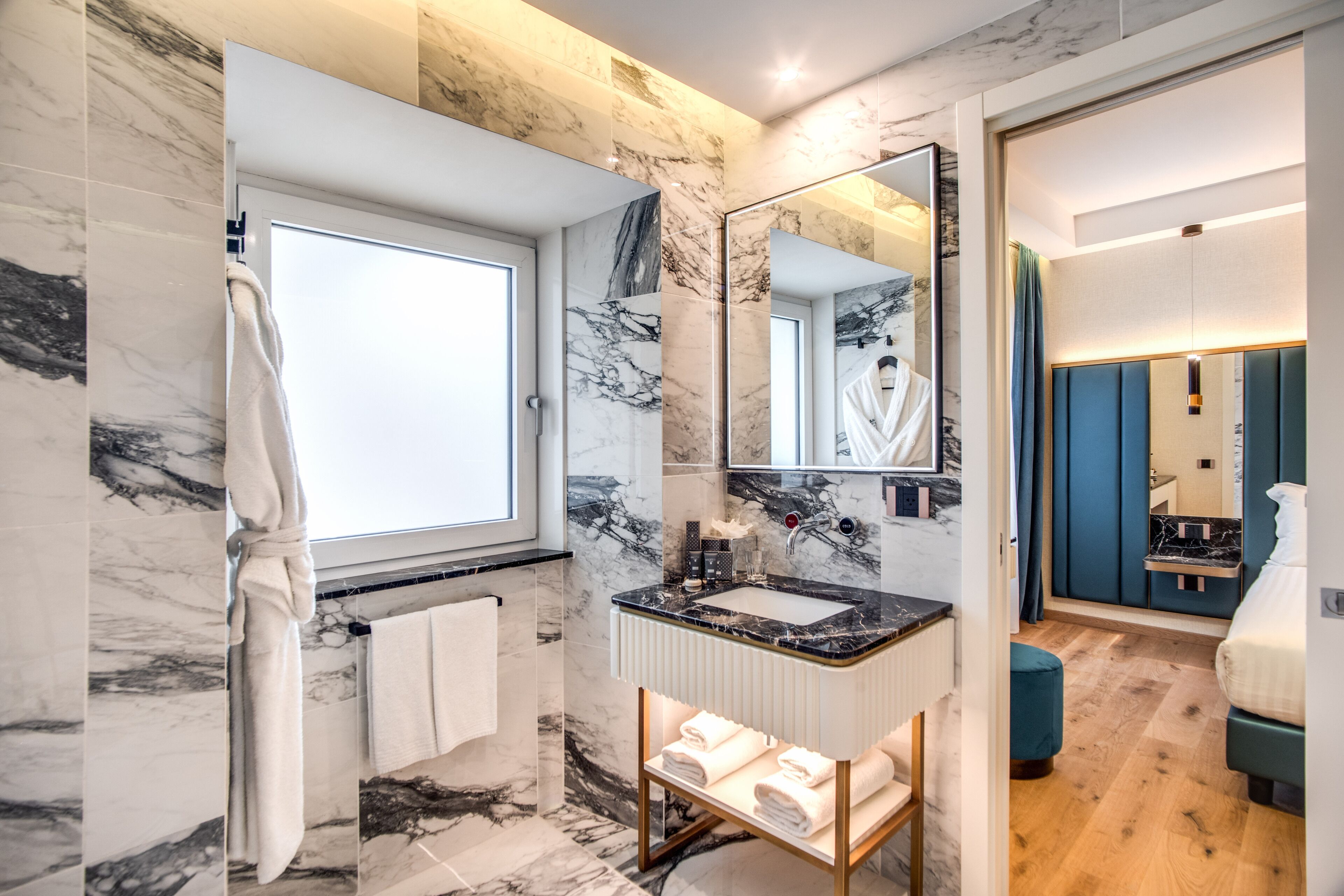 A modern bathroom with marble walls, a large mirror, a sink, and a wooden bench with towels.