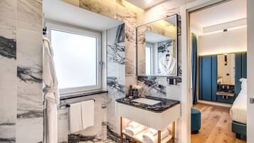 A modern bathroom with marble walls, a large mirror, a sink, and a wooden bench with towels.