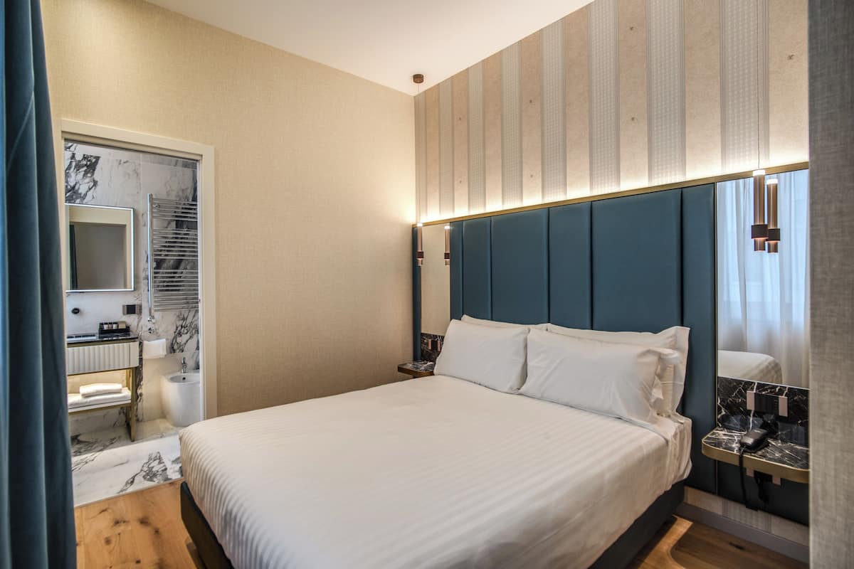 A hotel room with a bed, a bathroom with a mirror, a sink, and a towel rack.