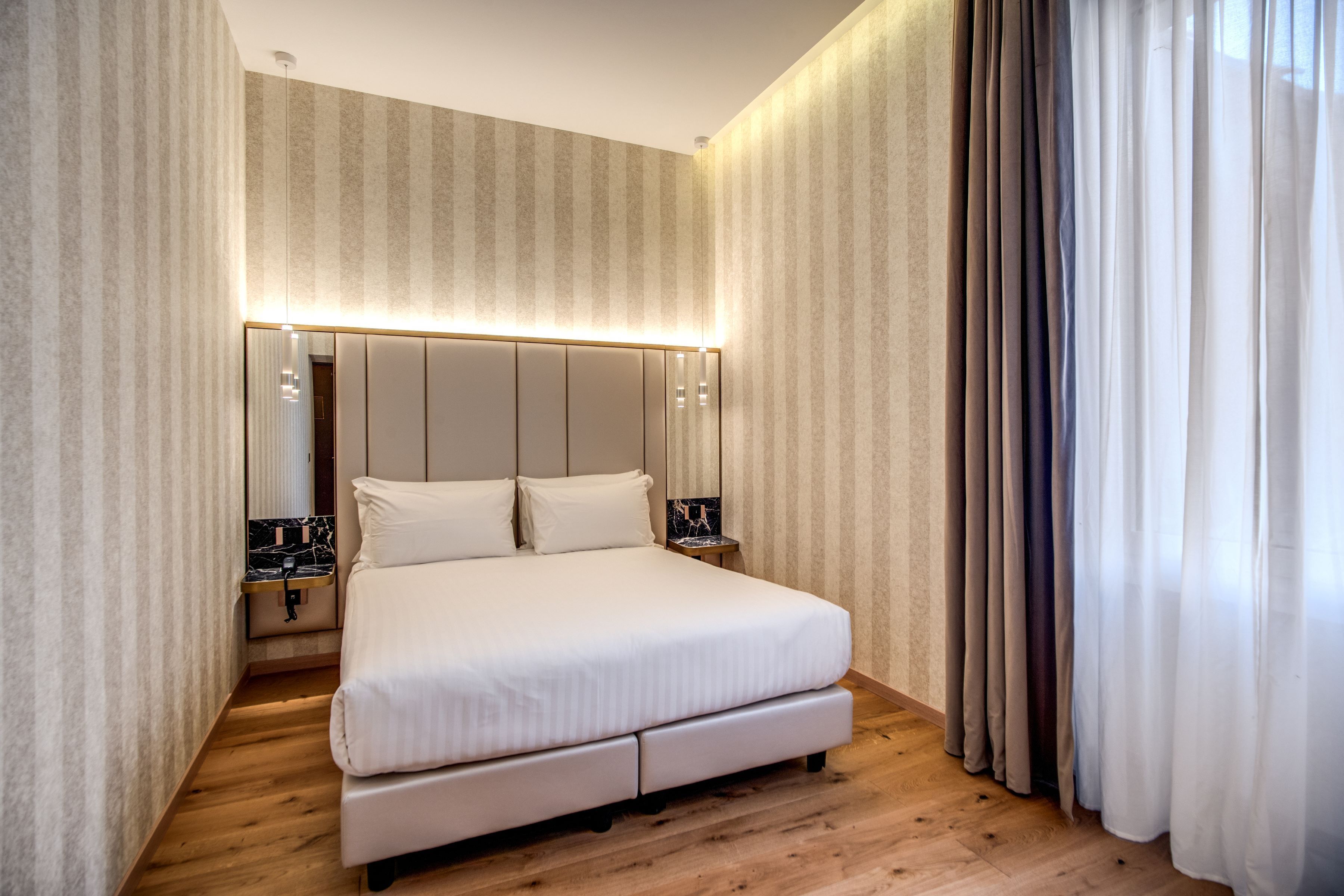 A modern bedroom with a large bed, wooden flooring, and striped wallpaper.