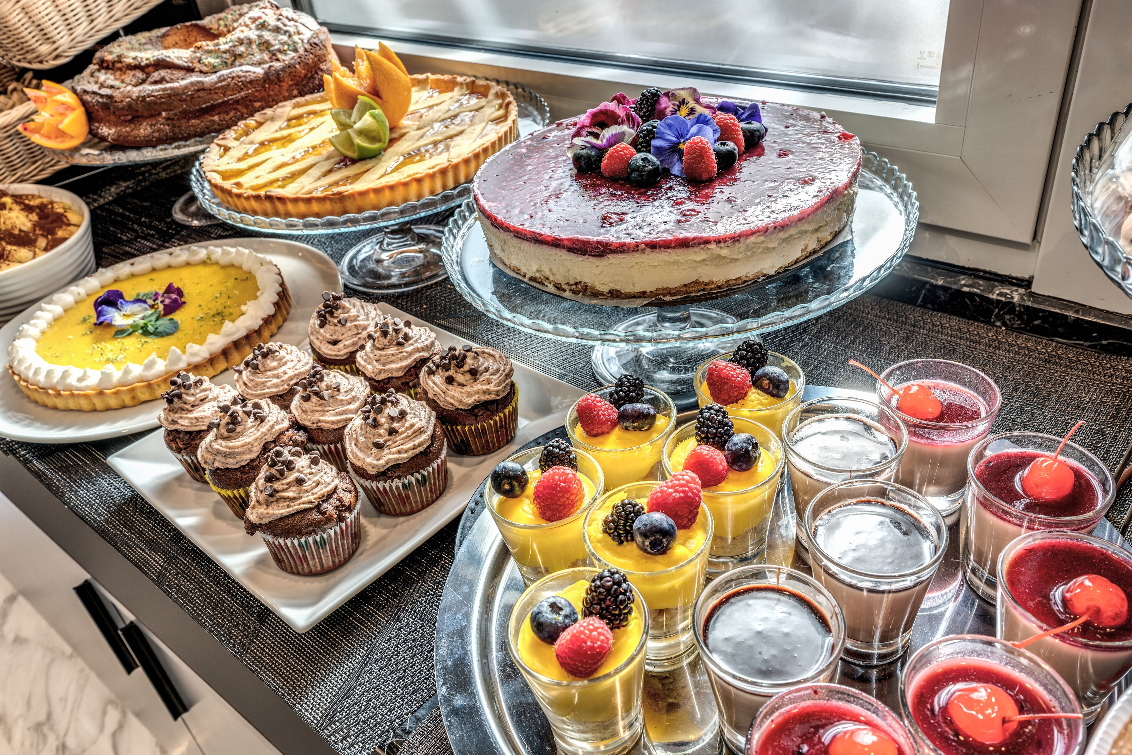A variety of desserts on display, including cakes, cupcakes, and fruit-topped drinks.