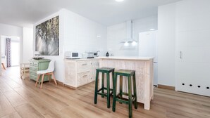 Uma cozinha moderna com armários brancos, piso de madeira e um banquinho verde.