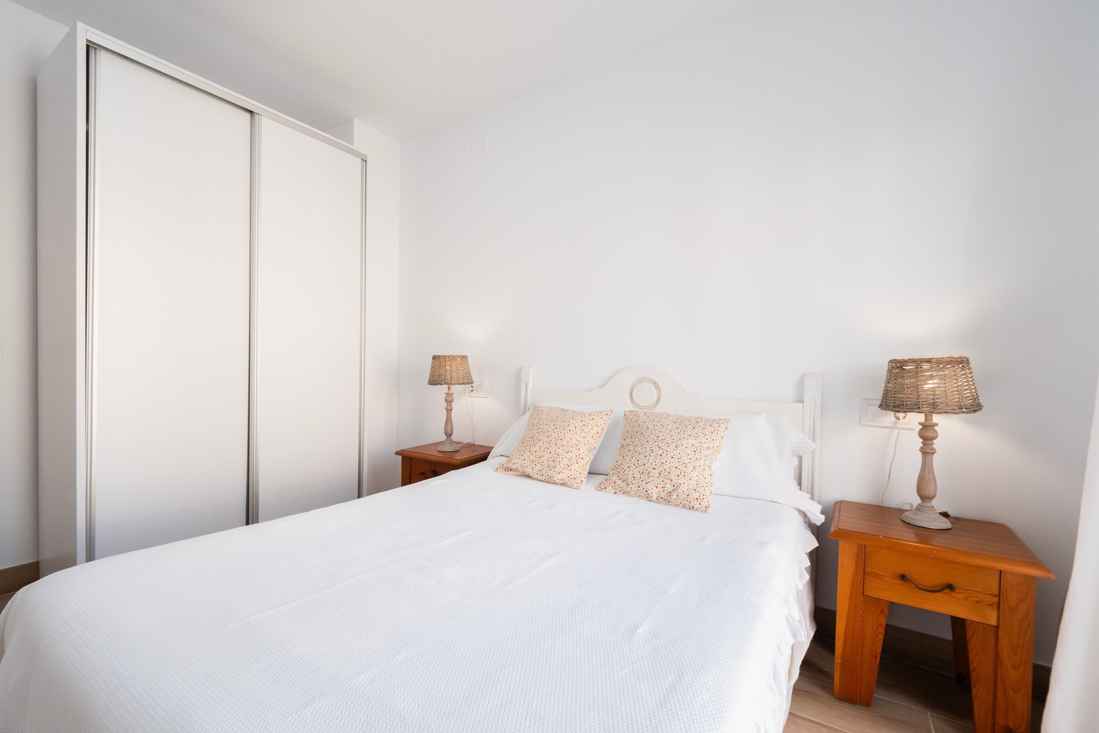 A bedroom with a bed, two bedside tables, a nightstand, and a wardrobe.
